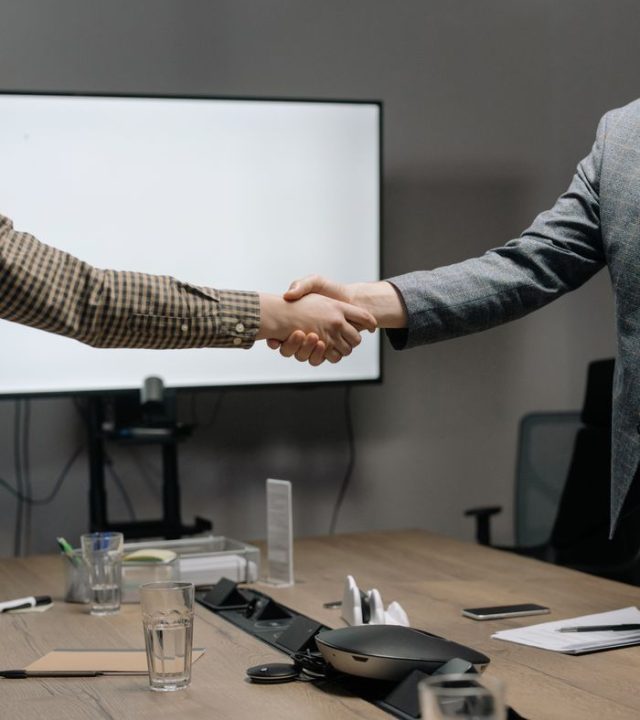 Two business professionals shaking hands in a modern meeting room, symbolizing successful collaboration.